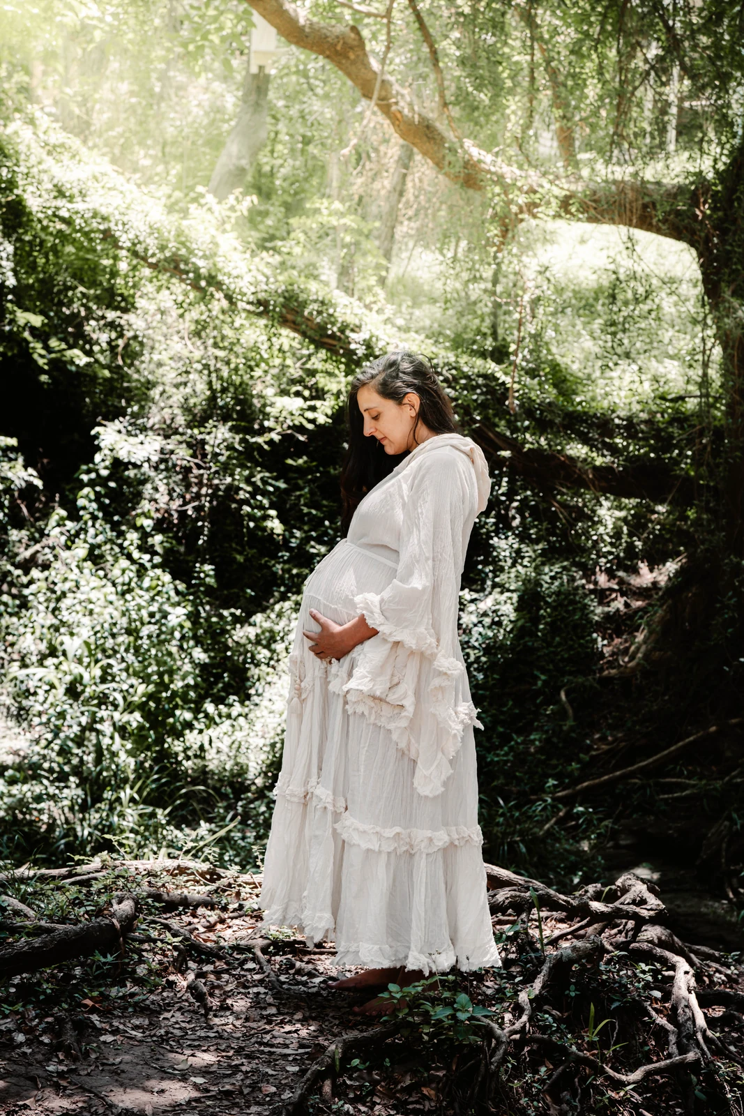 Ally cradling her bump in a sunlit forest