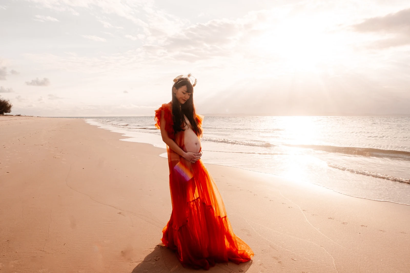 Maternity portrait in an orange gown on a sunlit beach